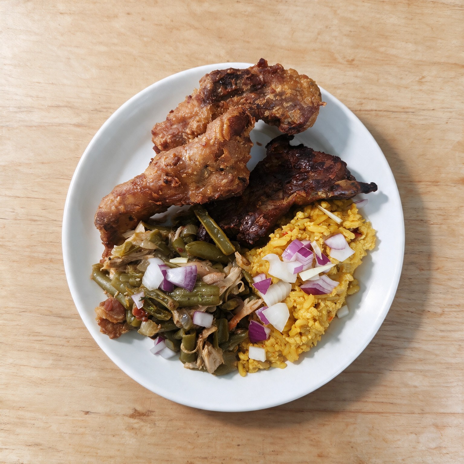 Crispy fried ribs served with seasoned rice and green beans on a white plate
